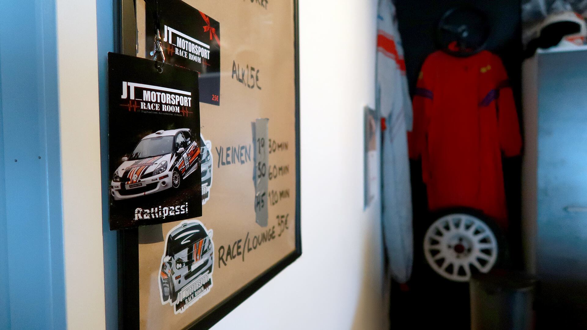 Yksityiskohta Race Roomin myyntitiskiltä. Kuvassa näkyy hinnasto, rallipassi sekä taustalla ajoasuja ja ralliauton rengas.
